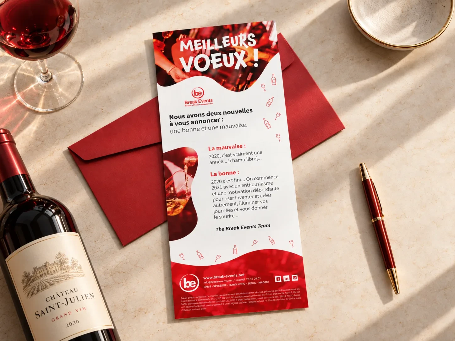 Carte de vœux Break Events posée sur une enveloppe rouge, avec une bouteille et un verre de vin.